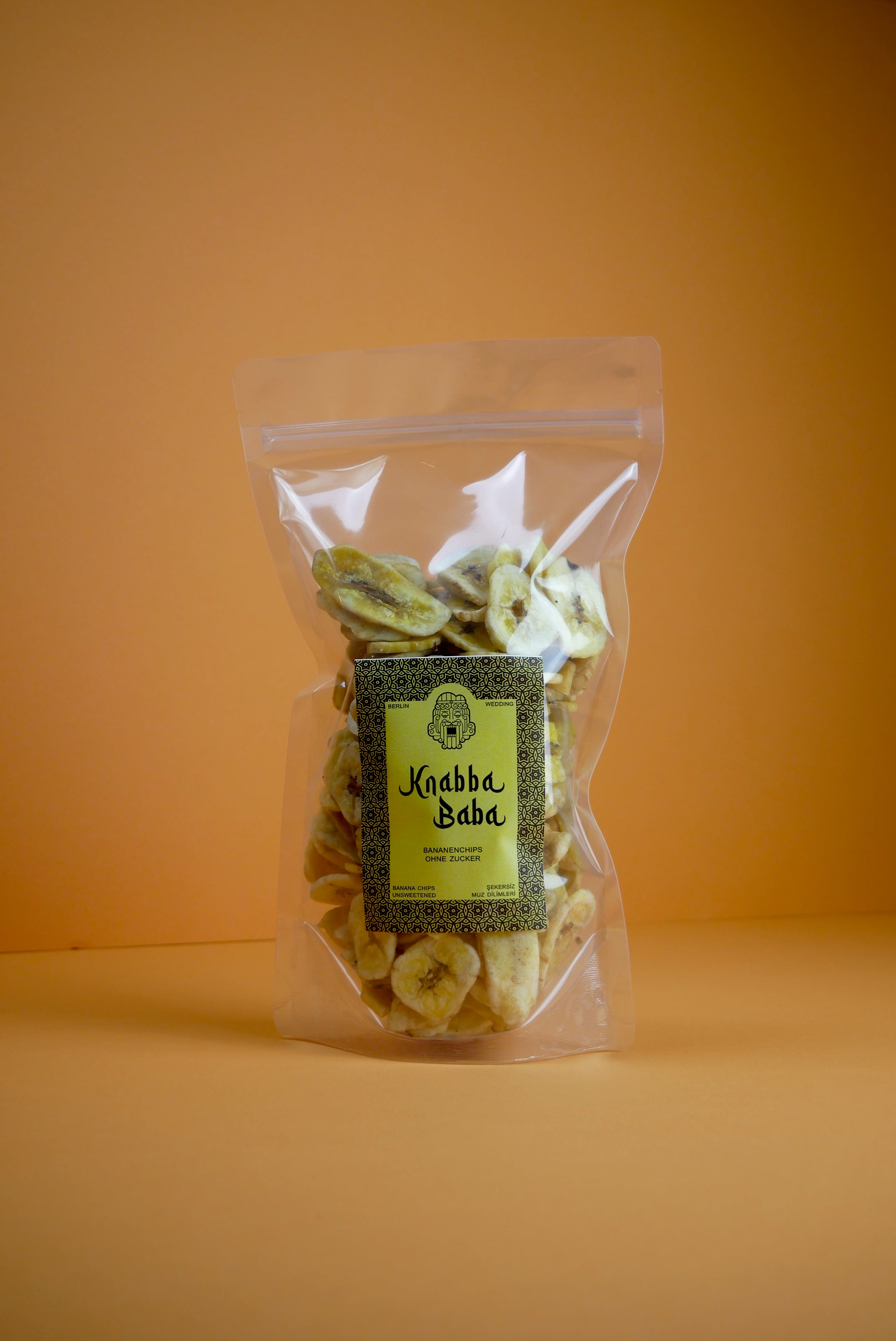Knabba Baba naturbelassene Bananenchips 250 g in Transparentverpackung vor orangefarbenem Hintergrund