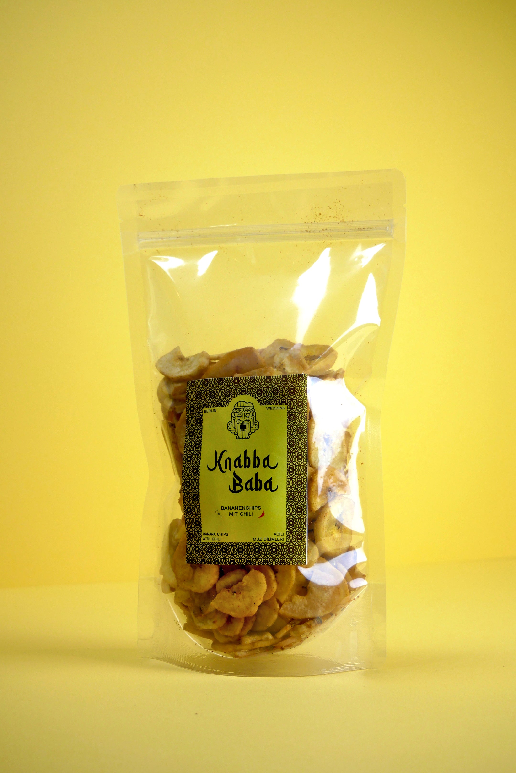 Knabba Baba getrocknete Bananenchips mit Chili 250 g in wiederverschließbarer transparenter Verpackung vor gelbem Hintergrund