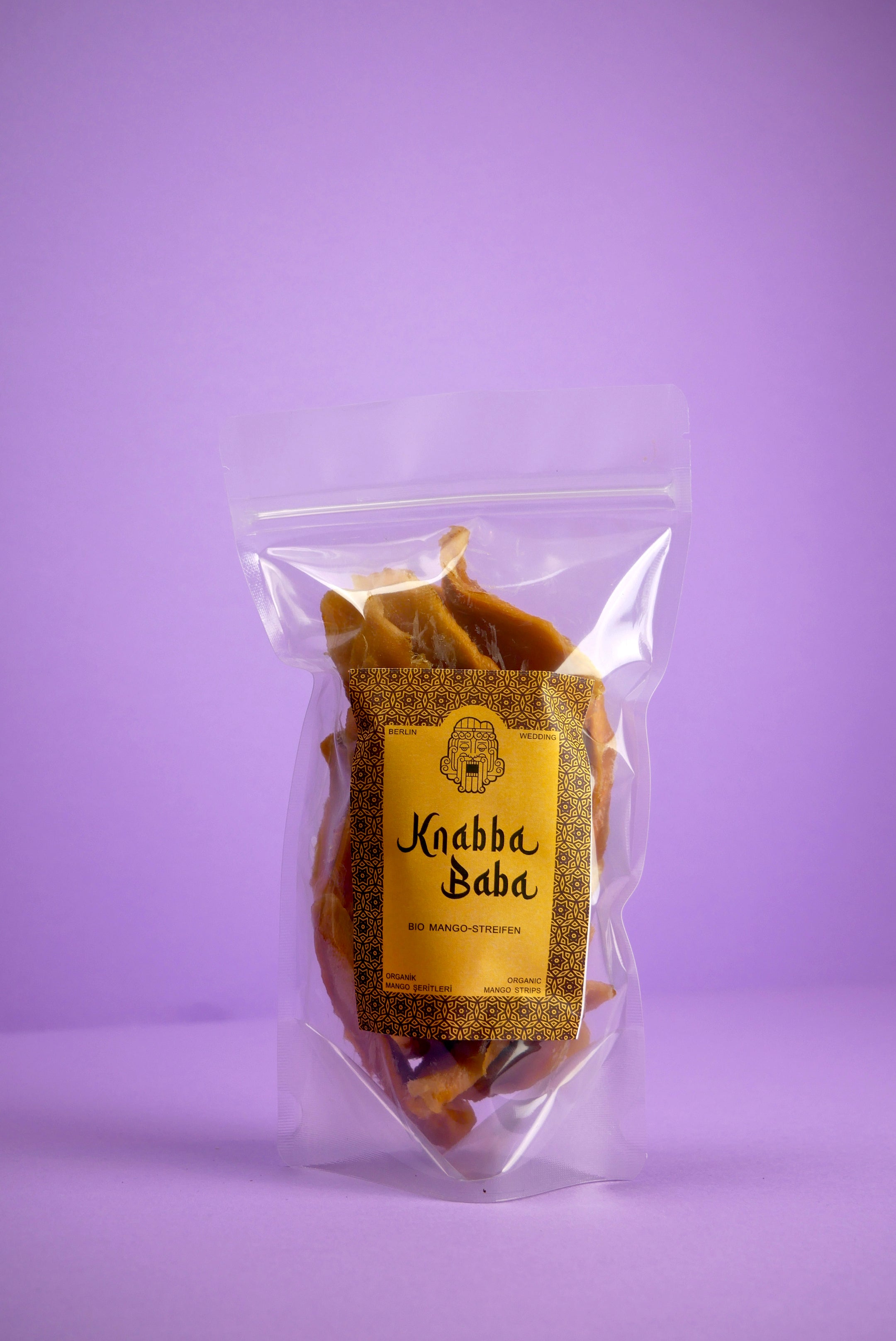 Knabba Baba Bio-Mangostreifen 250 g in wiederverschließbarer transparenten Verpackung vor lila Hintergrund