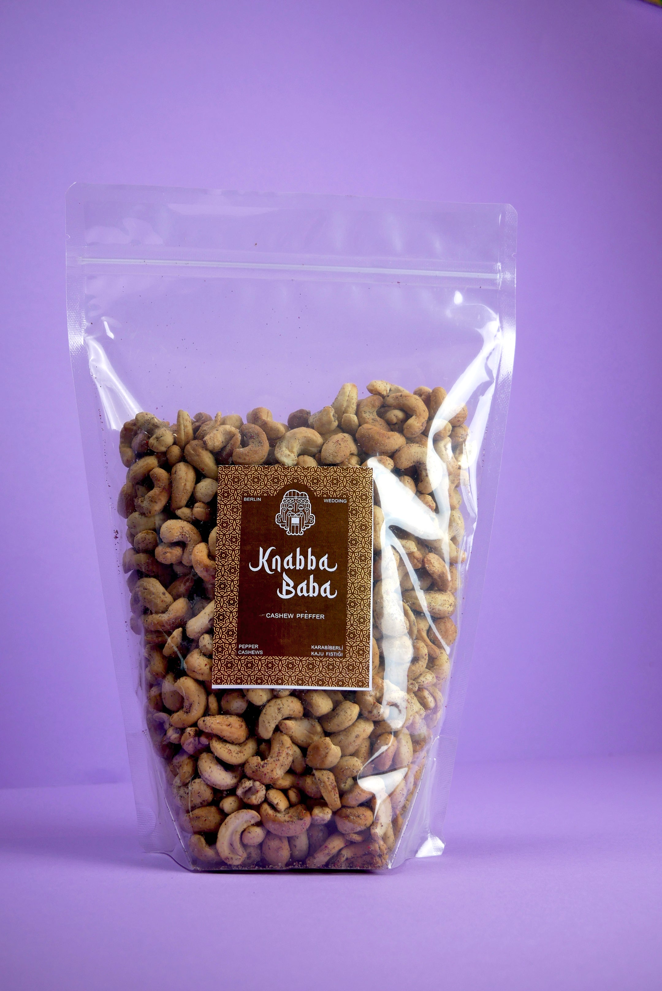 Knabba Baba handgeröstete Cashewkerne mit Pfeffer in wiederverschließbarer 1 kg Verpackung vor lila Hintergrund