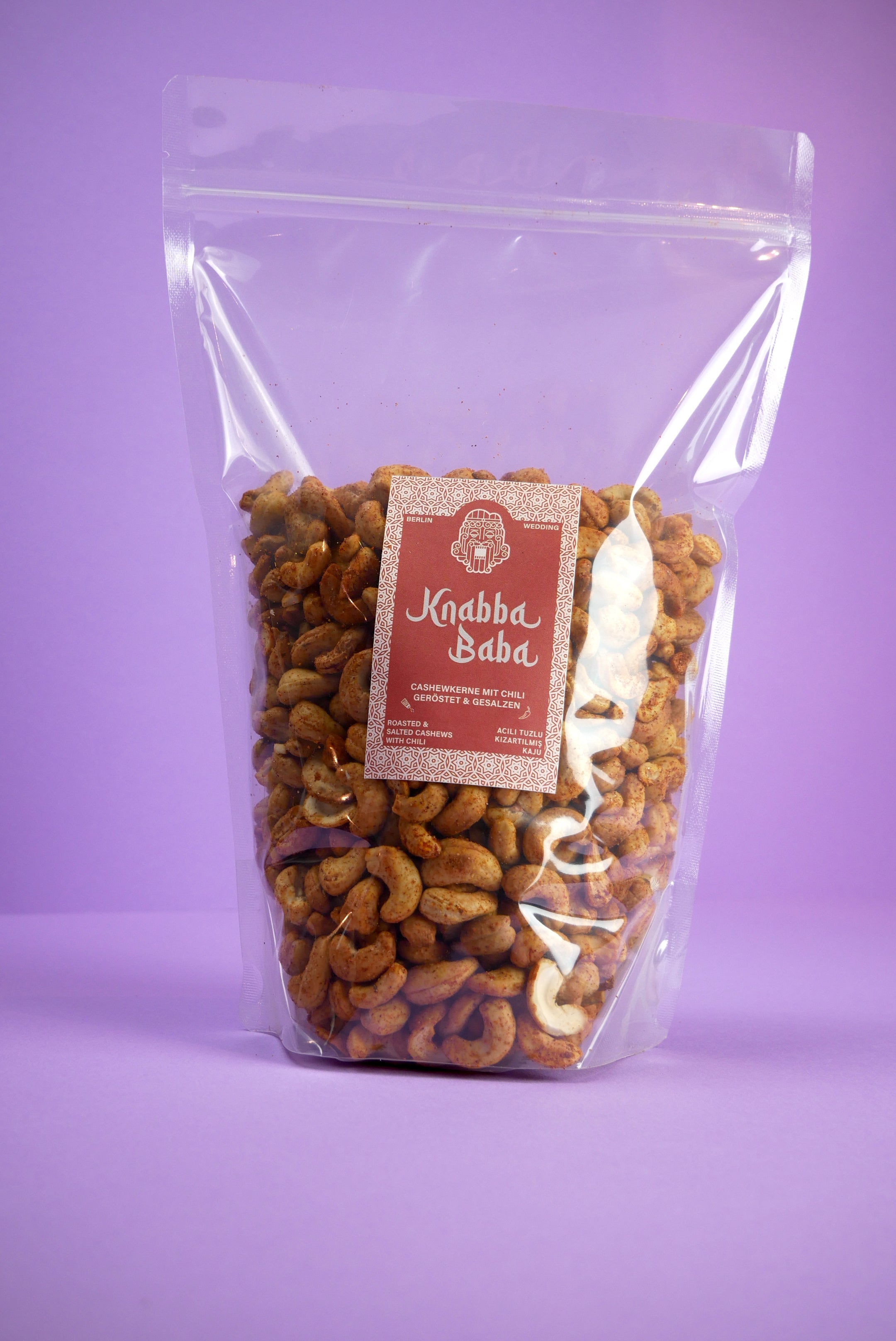 Knabba Baba Cashewkerne mit Chili 1000g in wiederverschließbarer durchsichtiger Verpackung vor lila Hintergrund