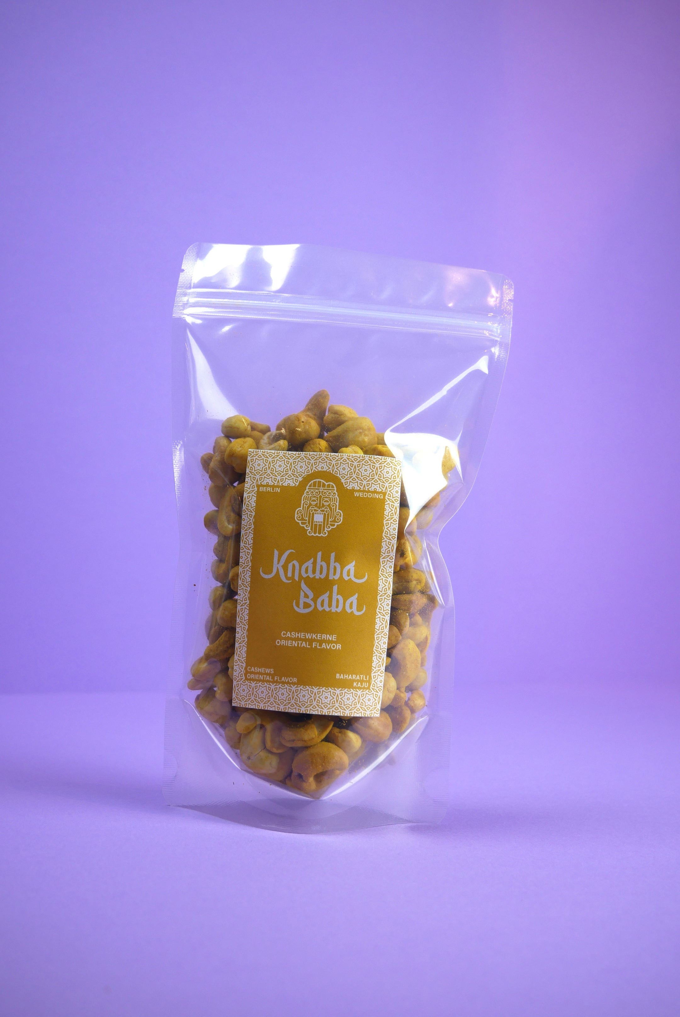 Knabba Baba geröstete Cashewkerne mit Curry 250g im wiederverschließbaren transparenten Beutel vor lila Hintergrund