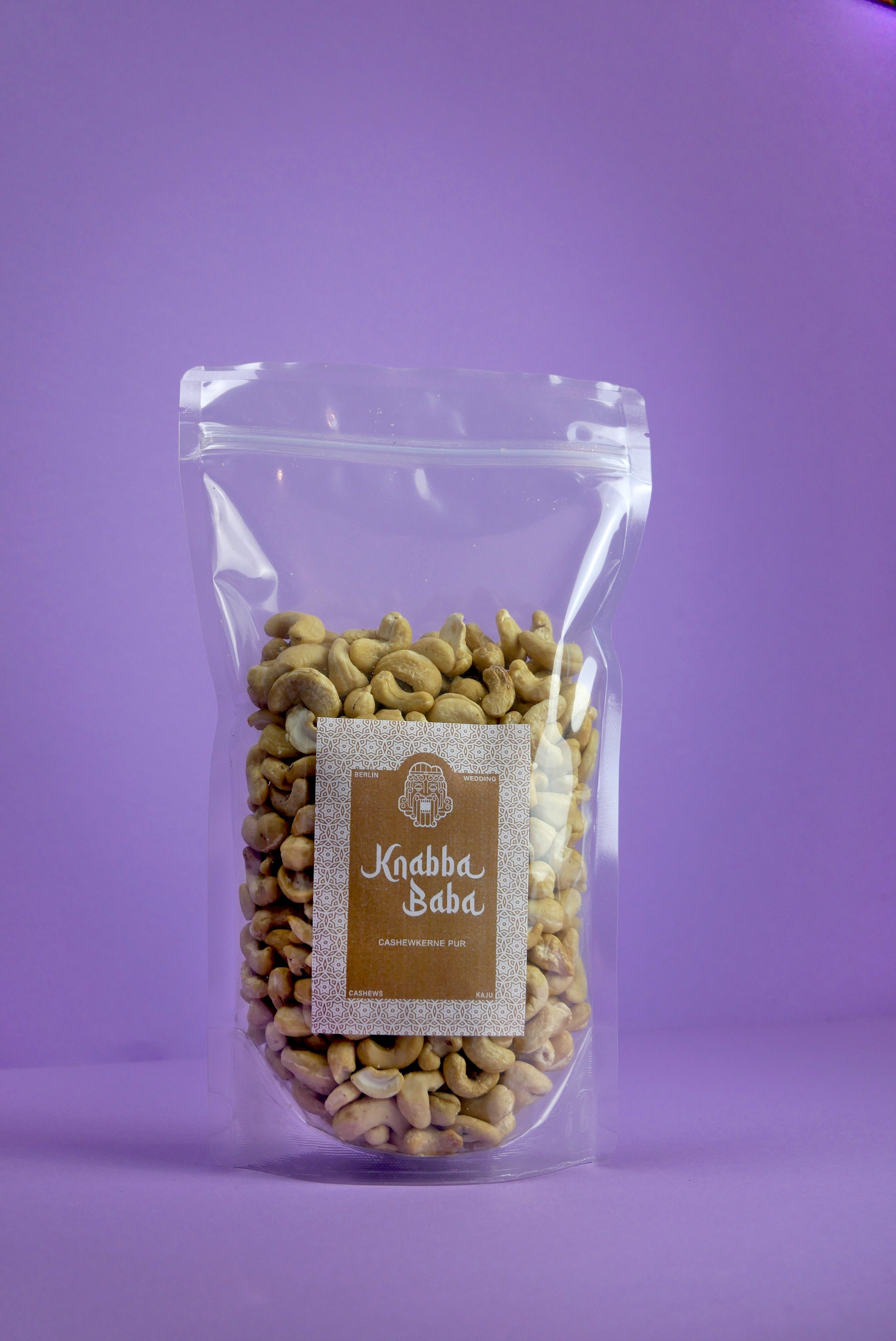 Knabba Baba Cashewkerne Premium 500 g im wiederverschließbaren transparenten Beutel vor lila Hintergrund