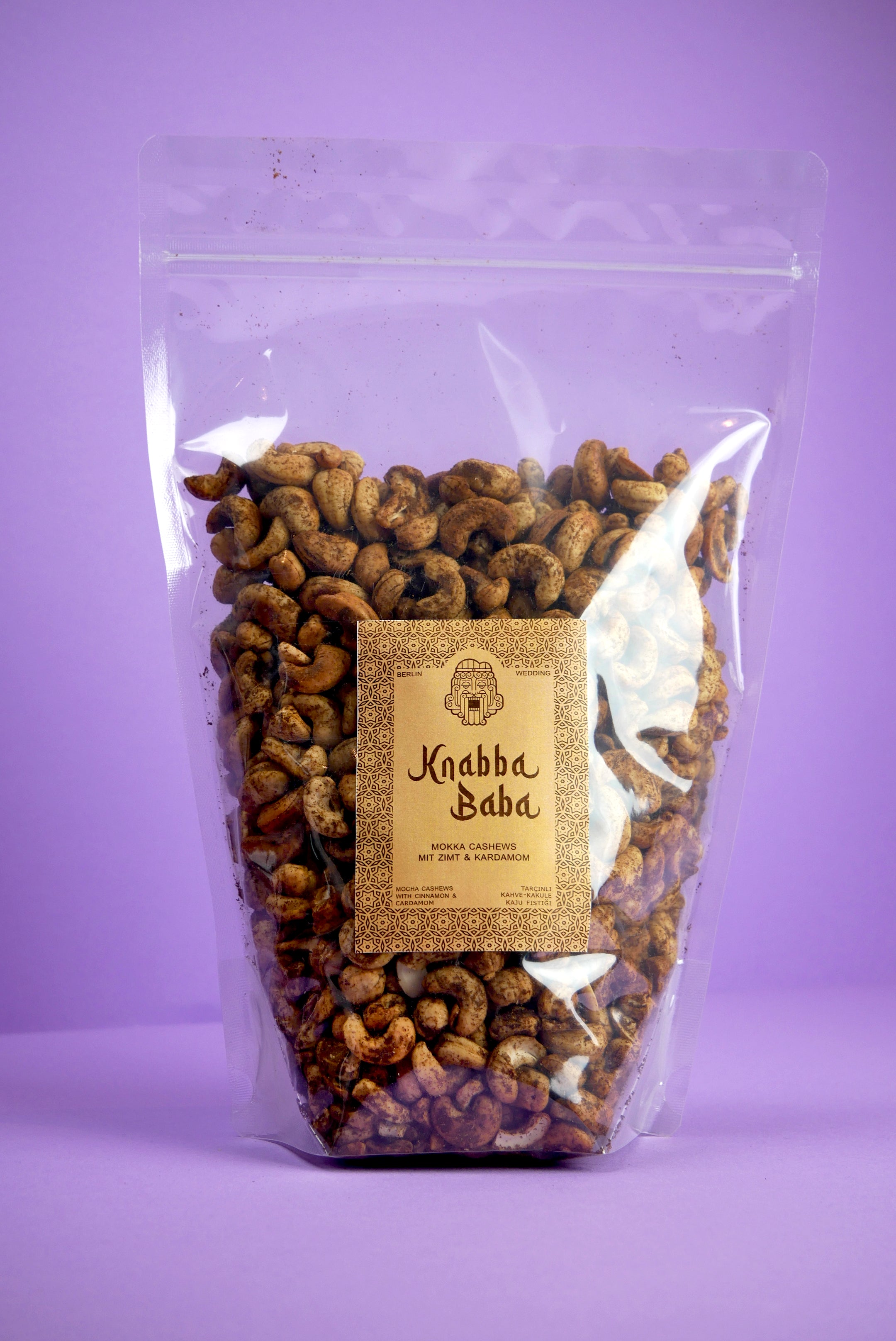 Knabba Baba 1 kg Cashews mit Zimt, Kardamom & Mokka  in transparenter wiederverschließbarer Verpackung vor lila Hintergrund