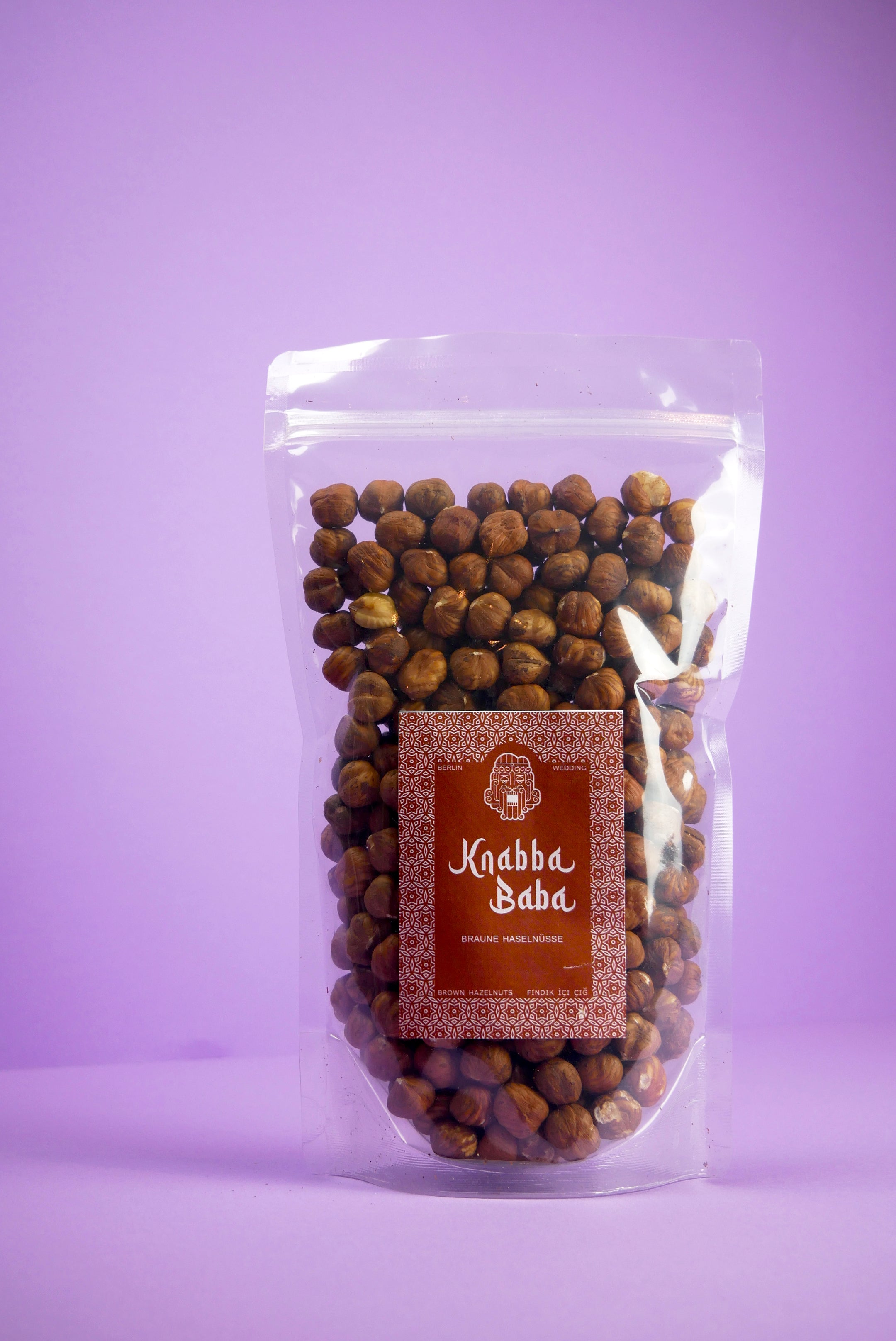 Knabba Baba naturbelassene Haselnüsse 1 kg in wiederverschließbarer transparenter Verpackung vor lila Hintergrund