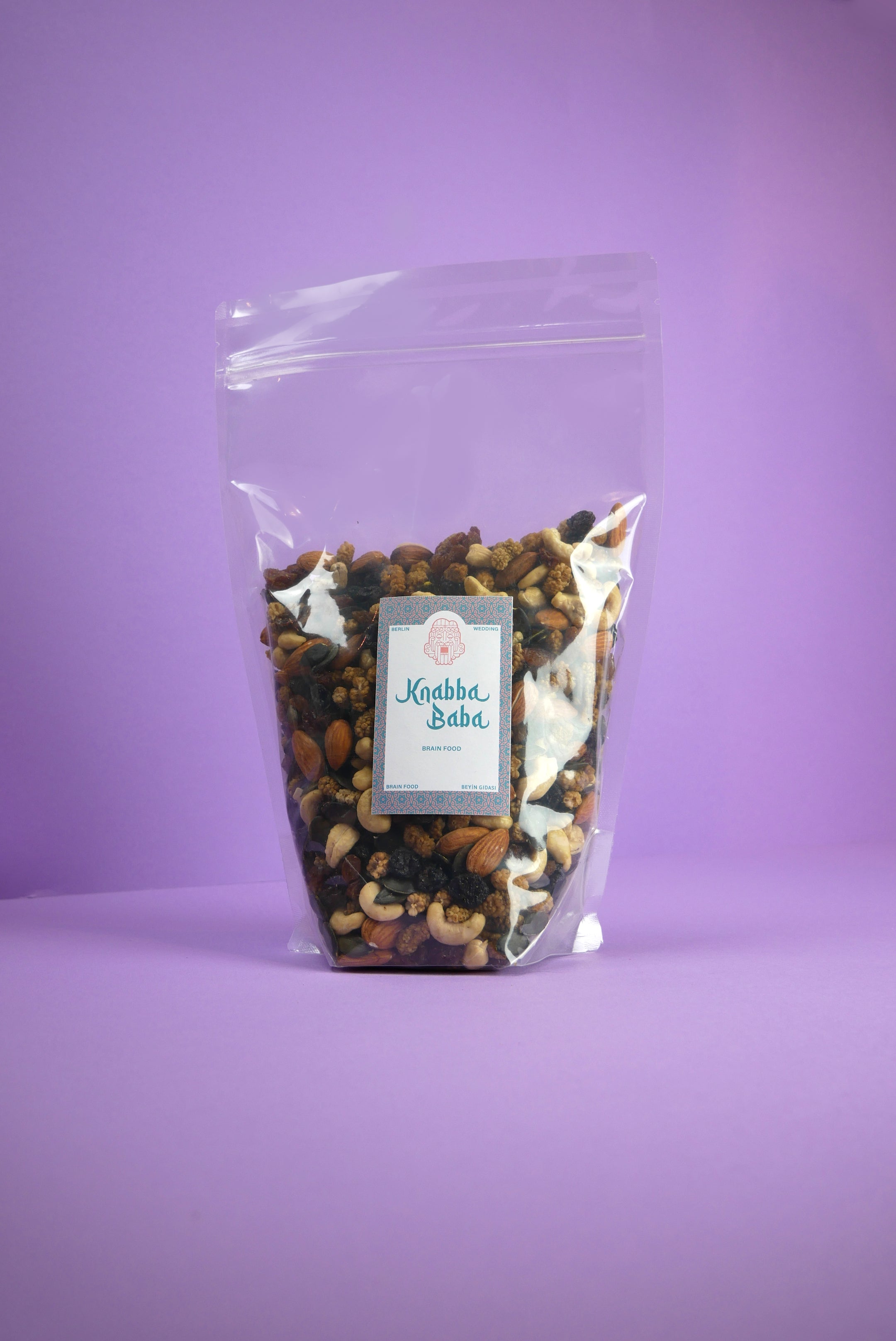 Knabba Baba Nussmischung Brain Food  1 kg im wiederverschließbaren Beutel mit verschiedenen gerösteten Nüssen vor lilanem Hintergrund